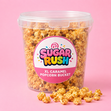 Sugar Rush XL Caramel Popcorn Bucket on a bright pink background with popcorn scattered in front